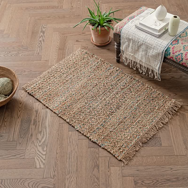 Woven natural area rug with fringe, featuring subtle multi-color threads, on a hardwood floor.